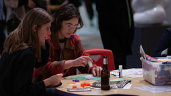 Two women collage and have drinks in the Discovery Gallery during our Summer 2023 Opening Reception.