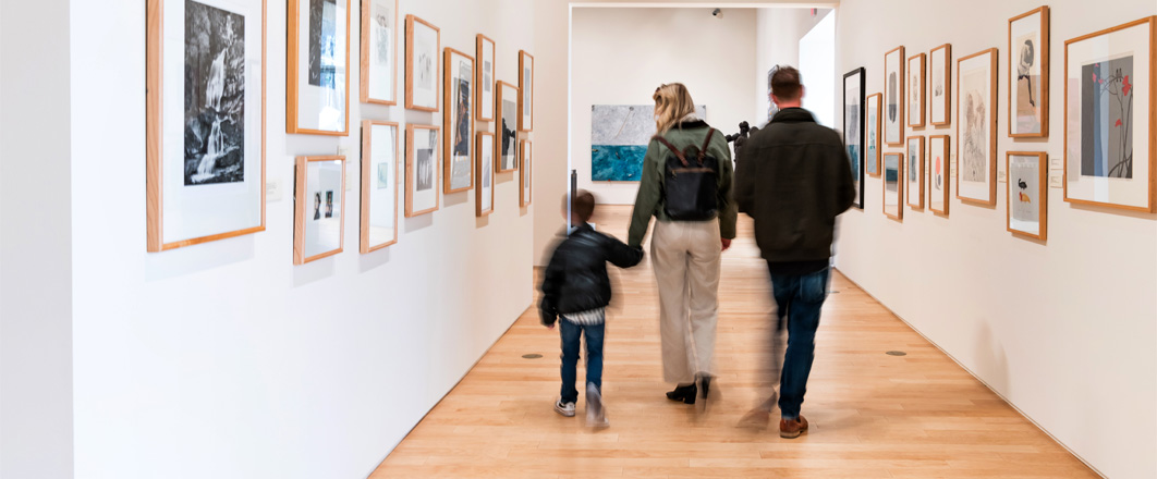 Installation view of the Jenneman Gallery at The Dennos featuring a family walking away from the camera.